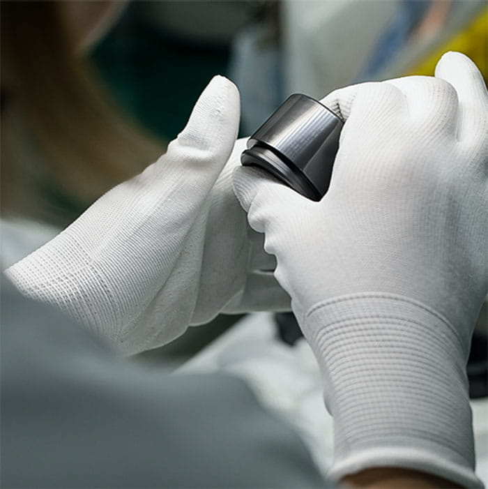 Expert technician in gloves performing quality checks on hard anodized components from the automated line.