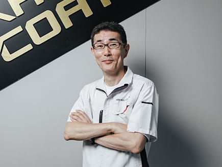 A professional Miyaki engineer in uniform standing in front of the Kashima Coat brand logo.