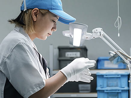 A Miyaki quality control technician wearing white gloves and a magnifying lamp inspects a treated component.