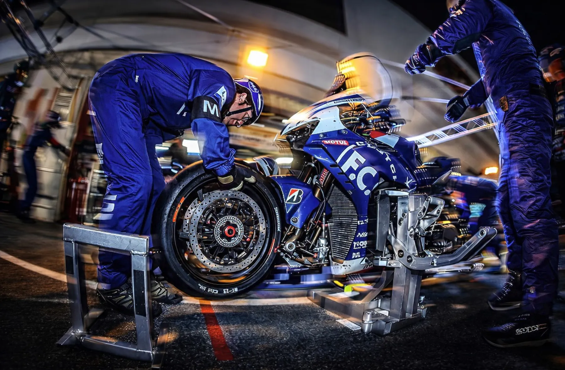 TSR mechanics performing a rapid front wheel change on a racing motorcycle during a night pit stop.