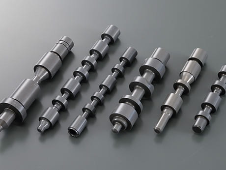 Multiple machined steel shafts treated with dark gray lubricating hard anodizing for improved wear resistance and durability.